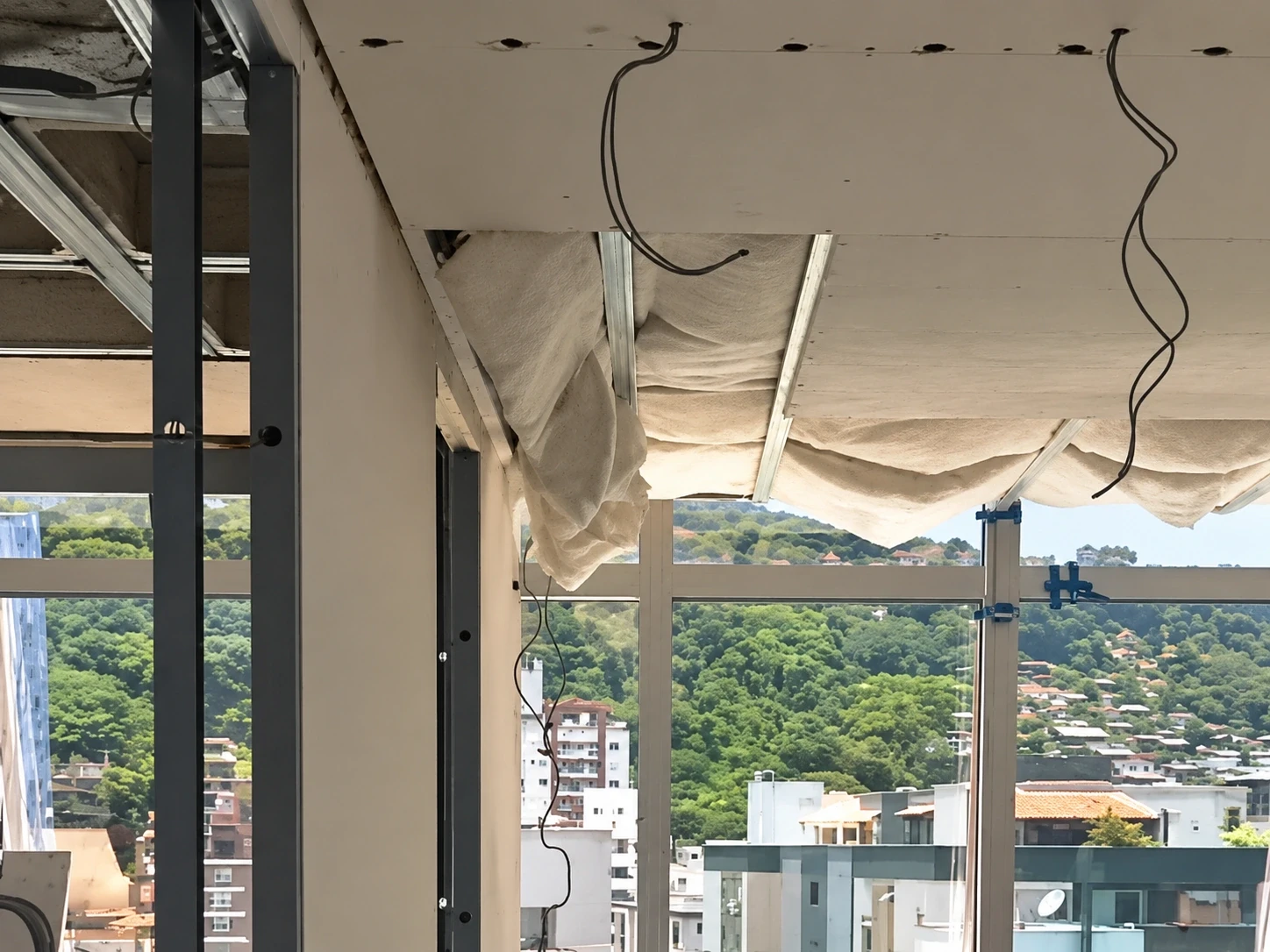 Forro de drywall em execução com cortineiro, isolamento em lã de PET e fiação para iluminação, com vista para o morro no Centro de Florianópolis