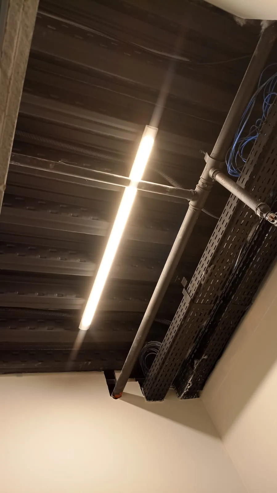 Corredor com teto aparente pintado de preto e luminária linear